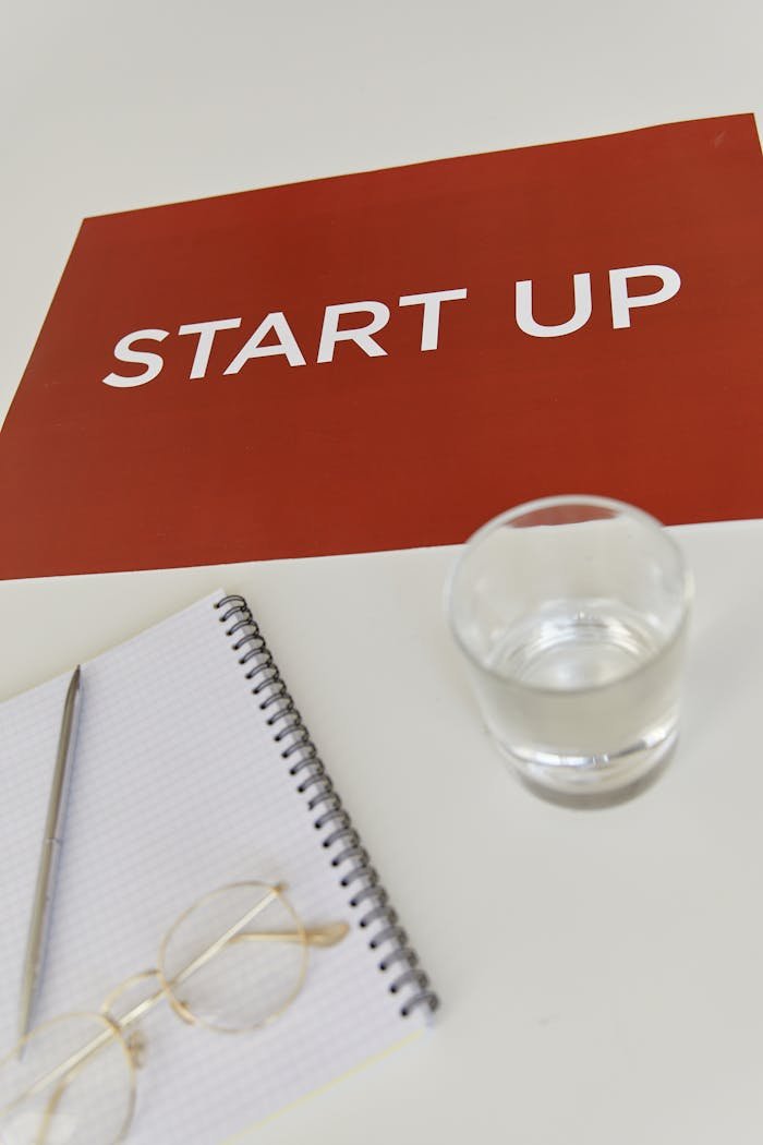 Red Poster Lying on Table by Notebook and Glass of Water